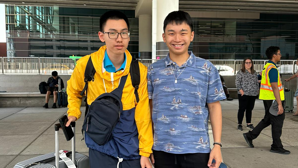 Hung and Hieu, two brothers from Vietnam studying at the University of Utah, stand at the airport with their luggage and smile for the camera