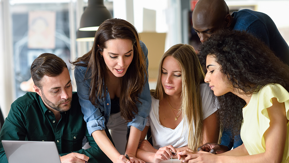 A group of international students working on a social sciences project at their US university huddle around a table to discuss an assignment.