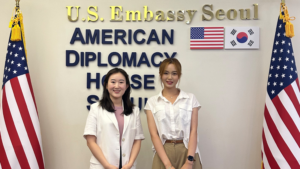 Somin, an international student from South Korea at the University of South Carolina, stands next to the US and South Korean flags at the U.S. Embassy in Seoul.