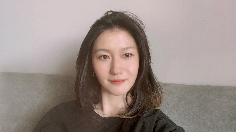 Sherry, an international student from China studying at Auburn University, sits on a gray couch and smiles for the camera