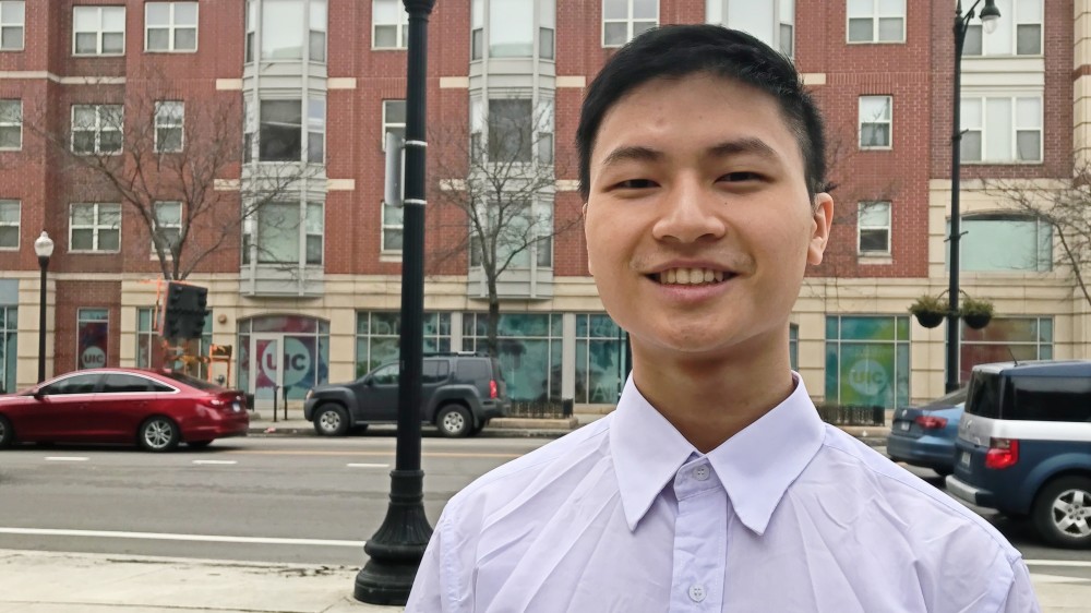 Huy, an international student from Vietnam, stands in front of a brick building and streetlamp on the UIC campus