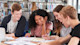 A group of international students sit together at a table in the university library and work together on an assignment.