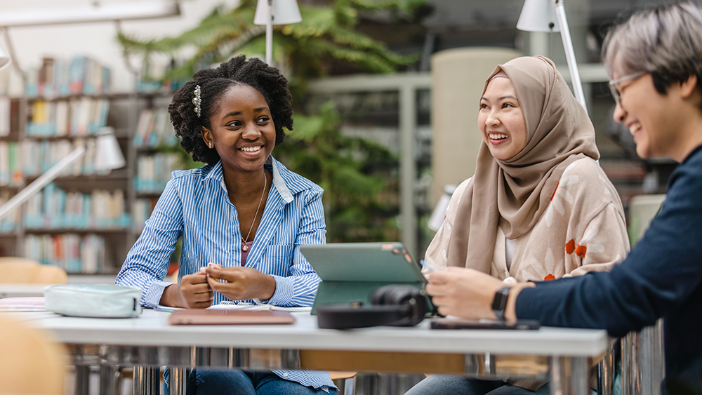 Two female international students who are studying to earn their PhD from a US university sit side by side in a university classroom building.