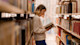 A female international student majoring in English literature stands among the stacks in her US university library and reads an open book.