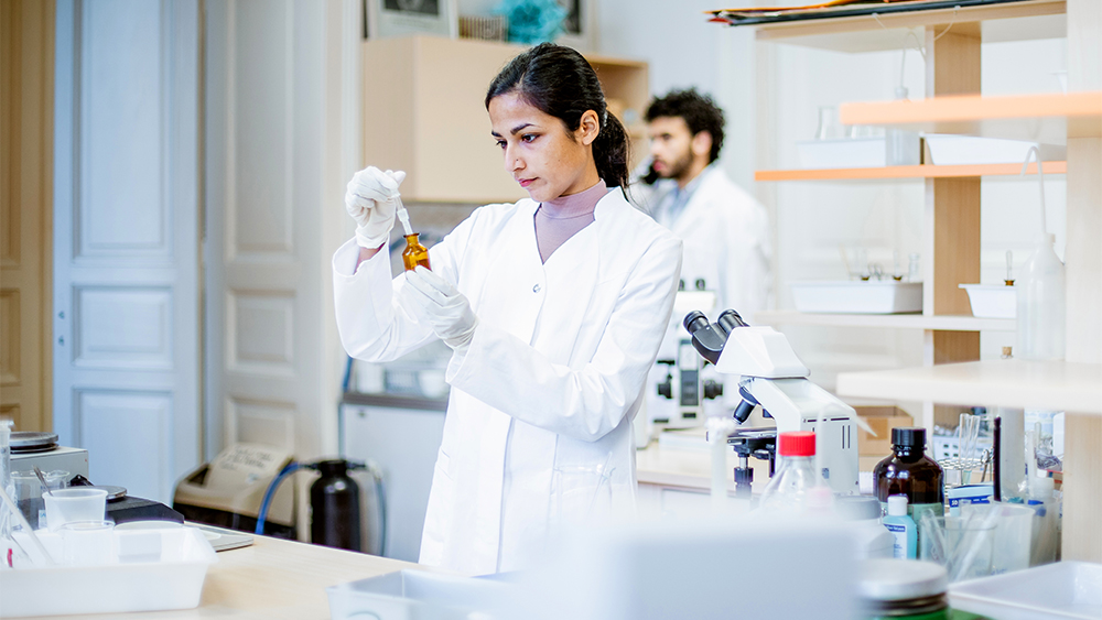 A female international student in a Pharm D program at a US university works in a lab on campus for an assignment for her pharmacist courses.