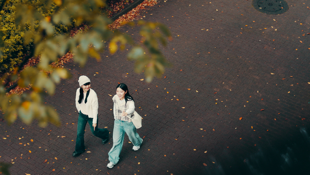 Two female Asian international students walk together on their US university campus and discuss self care practices and techniques.