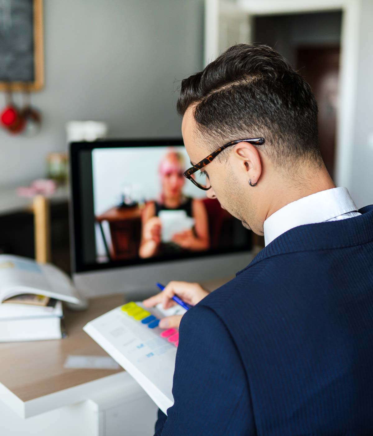 A male international student sits in front of an online class with an open textbook, his back to the camera, while studying at UDayton Live