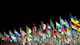 A row of international flags fly against a black background