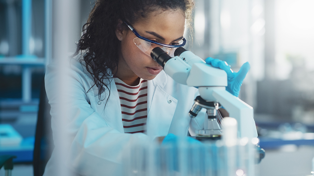 Female scientist wearing safety goggles examines samples under a microscope in a modern laboratory