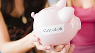 Two female international students hold out a piggy bank with the word COLLEGE taped on it