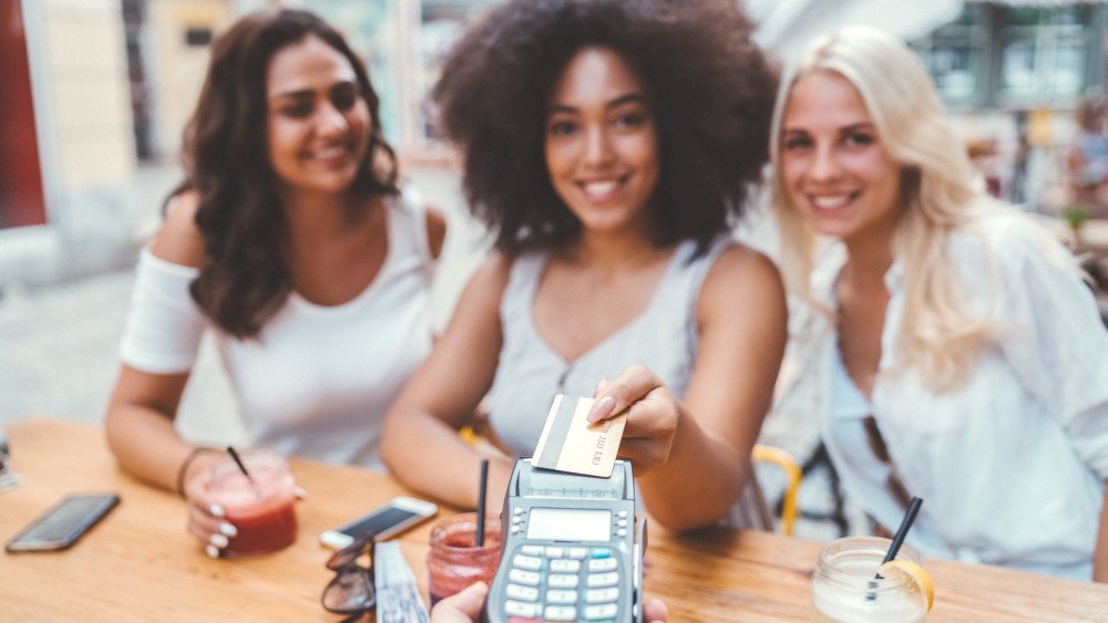 A student sitting at a restaurant table hands her credit card to her server.