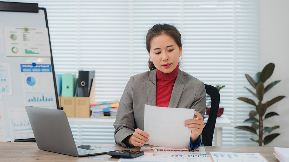 An Asian female student studying for a degree in business administration at her US university sits at a desk and studies a report.