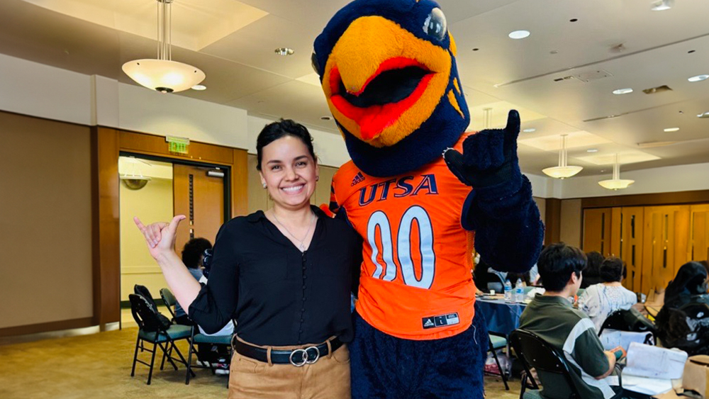 Leidy Bello Cristancho, student services advisor for international students at The University of Texas at San Antonio, stands with the Roadrunner mascot with both making the hand sign for UT horns. 