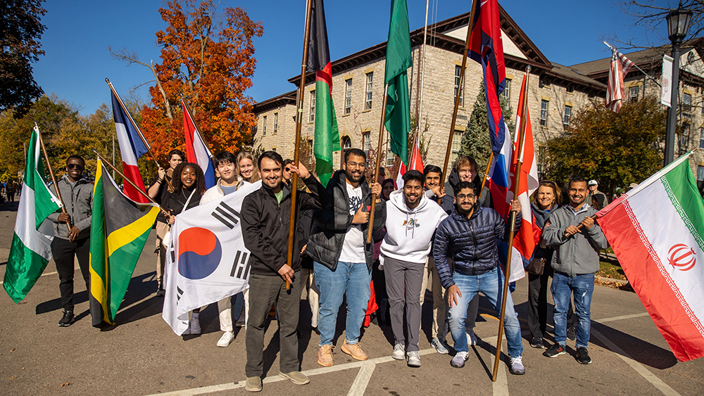 A group of international students at the University of Wisconsin-Platteville stand together on campus holding flags from their home countries
