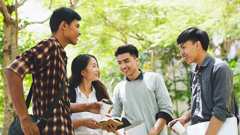 A group of Chinese international students sit outside at their US university and study together. 