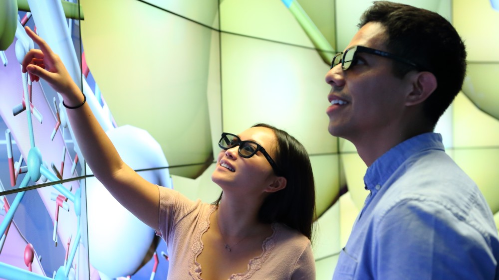 Two UIC international students wear sunglasses and stand by a wall with lit panels during an internship
