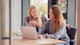 A female international student and her education counselor sit side by side at a table looking at an open laptop.