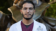 Ali, an international student from Saudi Arabia studying nursing at the University of South Carolina, stands in front of a statue of the school mascot on campus wearing a lab coat.