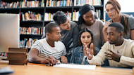 A group of international students earning their degrees in business administration sit at a table at their university library while working on a course project. 
