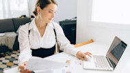A female international student sits at a desk at home and uses a laptop while working on an assignment for her corporate finance class