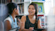 An Asian female international student sits at a table and speaks to a fellow female student about studying for a master degree in usa and master programs in usa. 