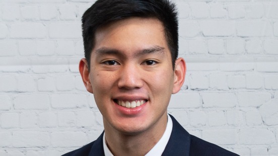 Saran, also known as Pitcher, an accounting graduate student at Gonzaga University in Washington State, sits in front of a white brick wall and smiles for the camera