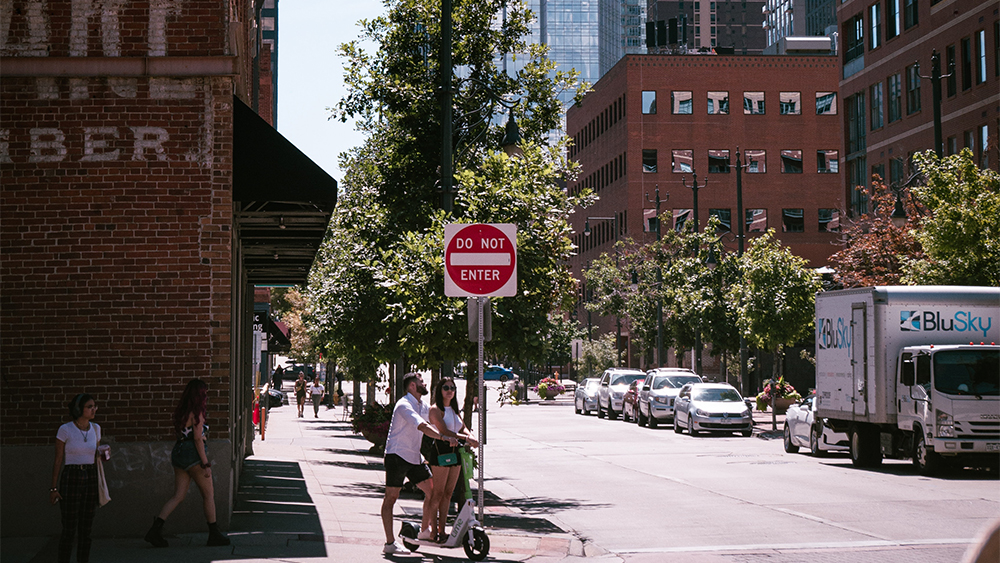 Two international students at Oklahoma City University stand with a scooter in a crosswalk downtown.