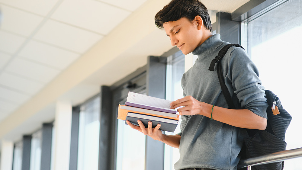 A male international student from Nepal stands in a hallway after his interview for a student visa USA from Nepal and consults his day planner.
