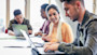 Four international students on laptops sitting at a classroom table working on assignments for their interdisciplinary studies at their US university