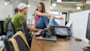 Two male college students sit across from a female college student sitting on a long table in front of a camera and a laptop at the University of Utah Lassonde Center