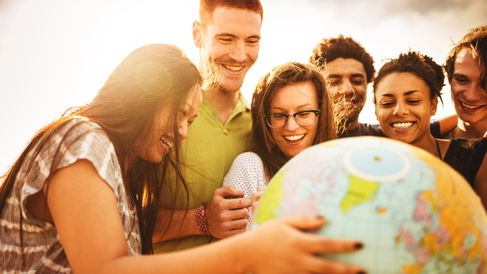 A group of international students studying international relations stand around a globe. 