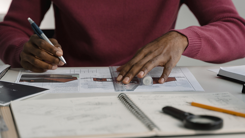 This photo shows the hands of an international student studying architecture in the US as they work on graphs and home design plans as part of their internship to build qualifications to become an architect. 