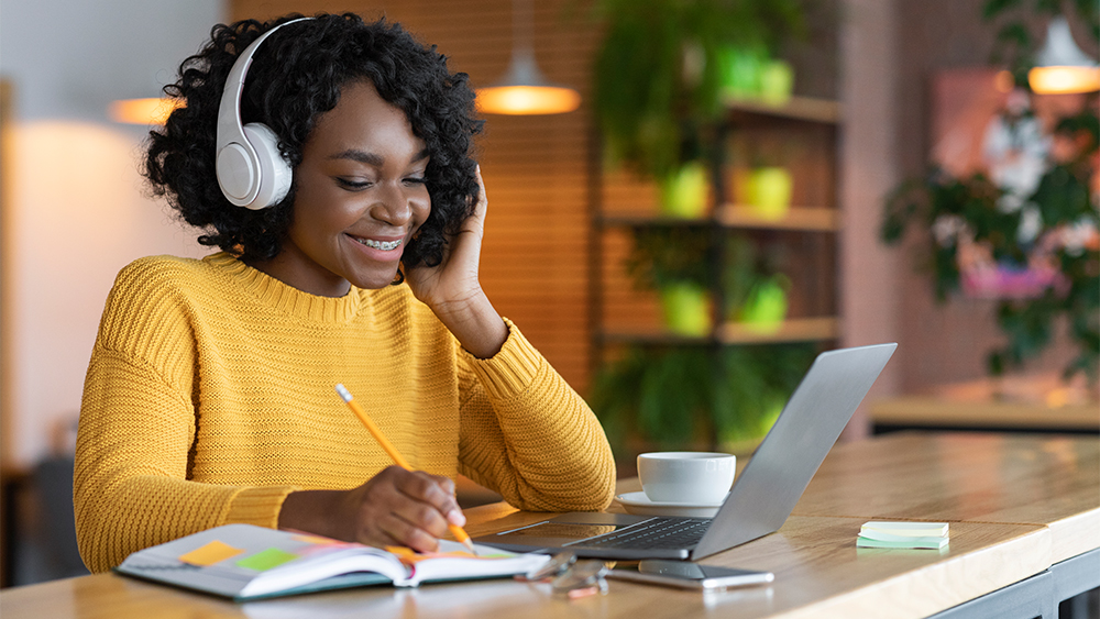 A female international student wears headphones and uses her laptop for a meeting with her tutor at Shorelight's Center for Academic Success