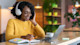 A female international student wears headphones and uses her laptop for a meeting with her tutor at Shorelight's Center for Academic Success