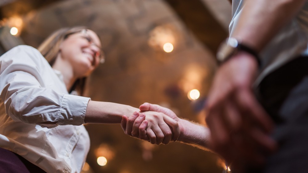 A young woman with glasses shakes hands with someone off camera as she requests a letter of recommendation to study in the USA