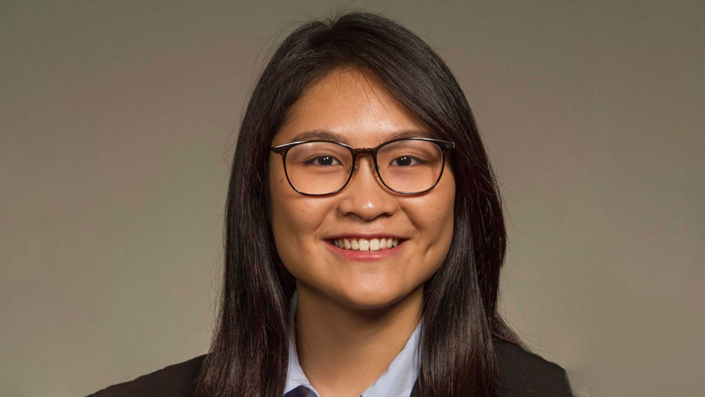 A headshot of Vy, a Vietnamese woman with long dark hair and glasses, smiling at the camera