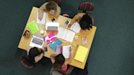Four female international students studying together at a table, taking notes and talking to each other.