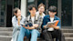 Four international students from Indonesia sit on the steps of their US university library and work on an assignment together.