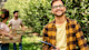 Three international students in an agriculture course at US university work in a field, with one student in front smiling with a clipboard while two in the background pick produce.