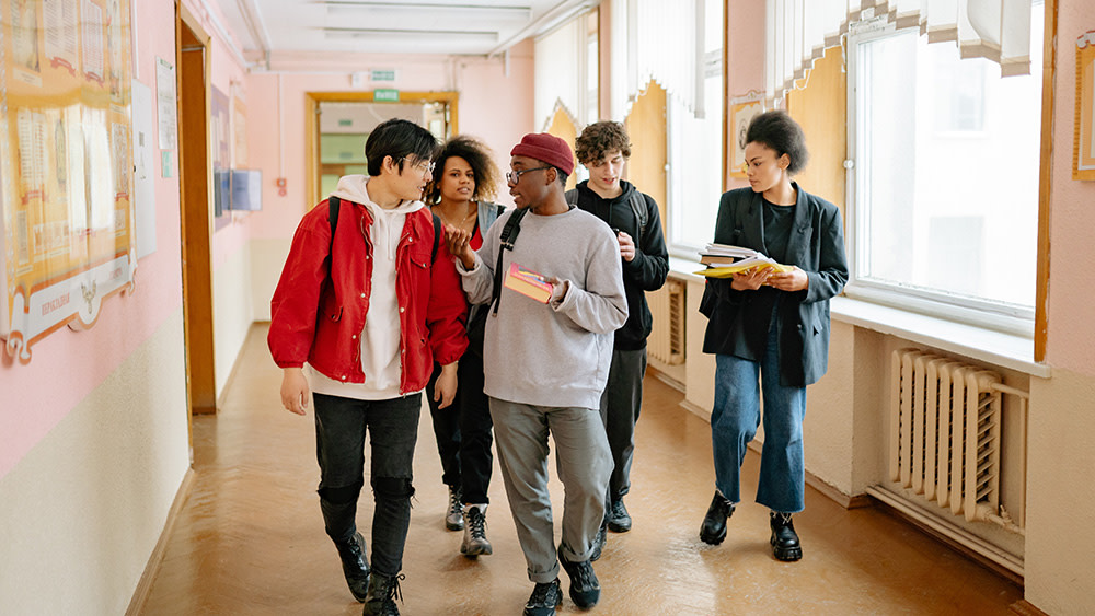 As part of the daily routine for students, a group of five international students walk through a corridor at their university, talking to each other.