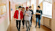 As part of the daily routine for students, a group of five international students walk through a corridor at their university, talking to each other.