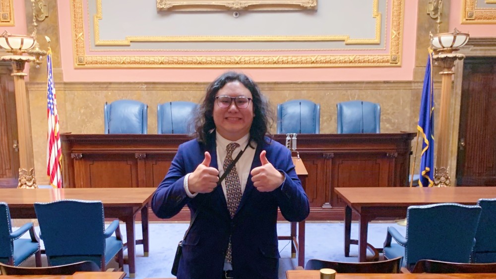 Billie, a Utah Global student from Thailand, stands in front of a desk at the Utah State House during his internship for the Utah State Attorney General