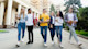 A group of international students holding textbooks walk and laugh together on a city campus