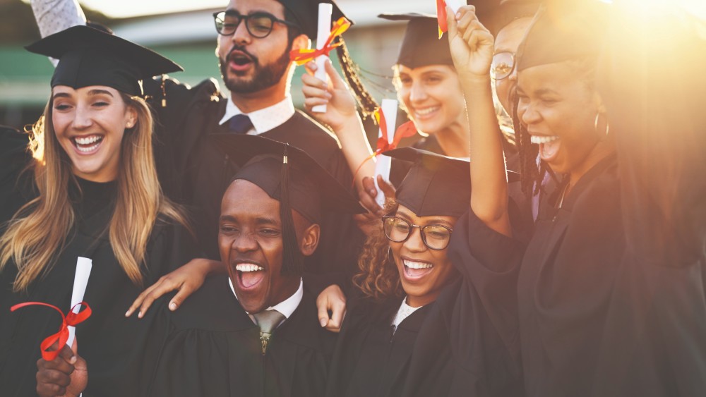 A group of international students dressed in caps and gowns for their university graduation hold their diplomas and smile for the camera