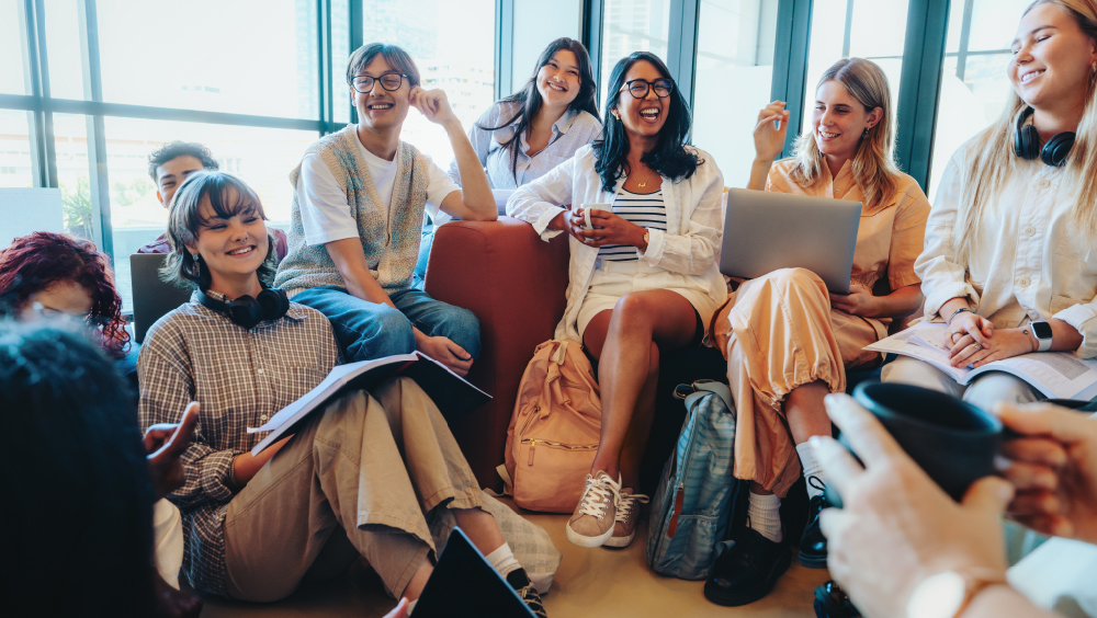 A group of international students sit together in a student lounge at their US university, laughing mid-conversation.
