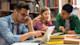 A group of three Canadian students sit at a table with laptops preparing their student visa USA from Canada.