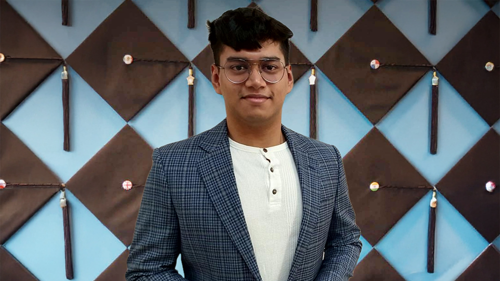 Fardeen Shaikh, a graduate of Heriot-Watt University Dubai and a member of Shorelight's global product sales team, stands in front of a wall of graduation caps at the Shorelight office and smiles for the camera.