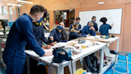 Six international civil engineering students wear safety overalls and facemasks at a work table discussing civil engineer jobs and civil engineer salary options with each other.