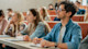 Students sitting in a lecture hall, listening attentively and taking notes at their desks