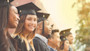 After learning about the American education system, the definition of higher education, and earning their higher ed degree from the US education system, six students wearing graduation caps and gowns stand while a woman in the middle smiles at the camera. 